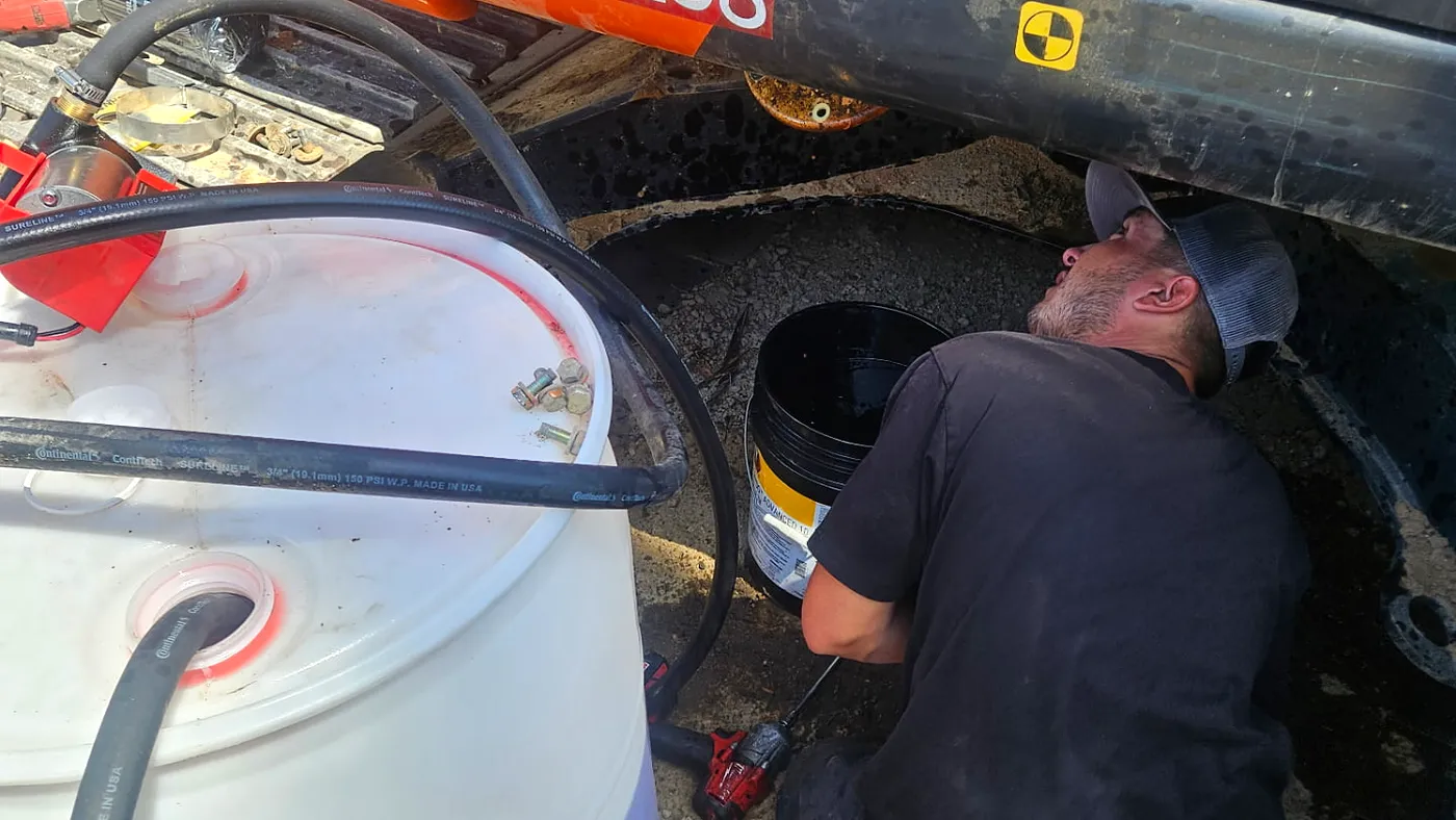 Technician performing a repair underneath an excavator at a jobsite